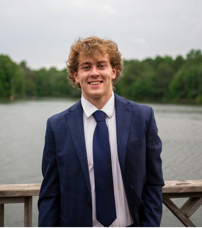 Nash Davis, standing on a dock by a lake in a navy suit