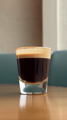 A glass of espresso on a café table, vertical