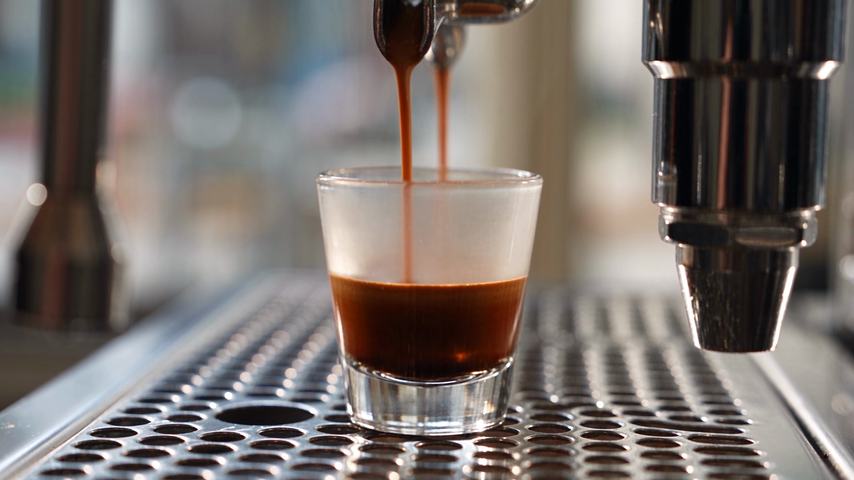 An espresso machine pouring a shot into a small glass on the drip tray